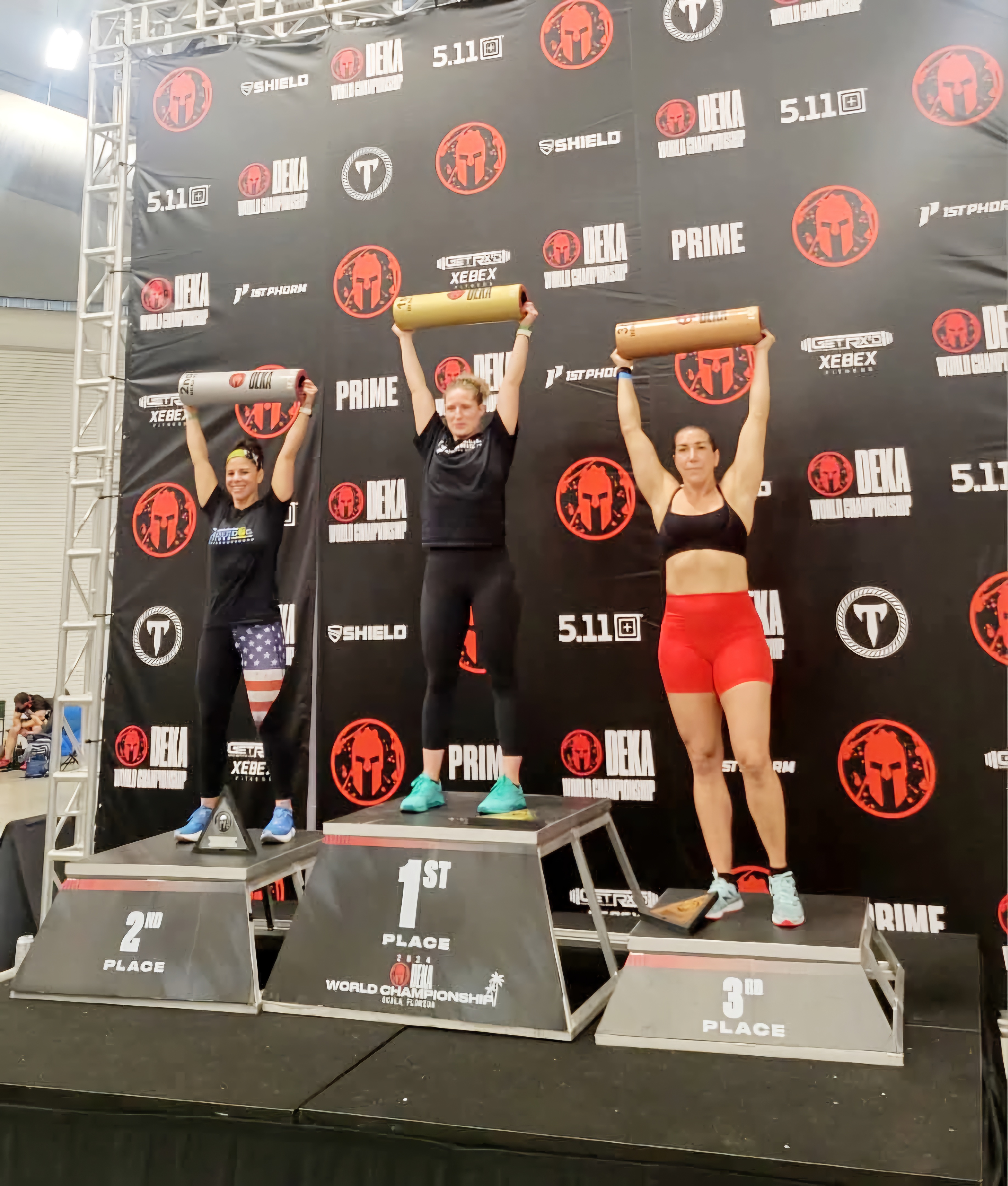 Photo of 3 women on a podium - 1st, 2nd and 3rd. Fitness competition.